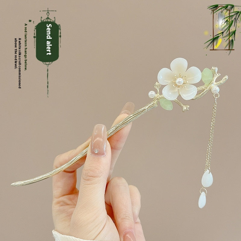 Hand holding a decorative hairpin with floral design against a beige background