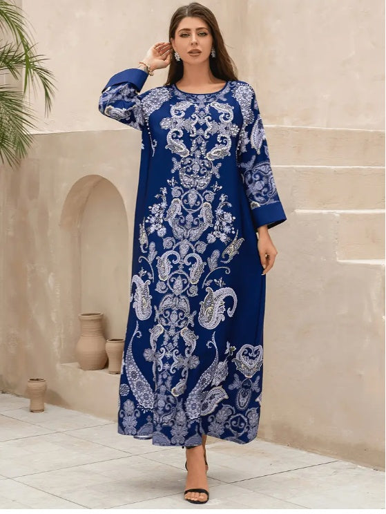 Woman wearing a blue and white patterned dress standing against a beige wall.