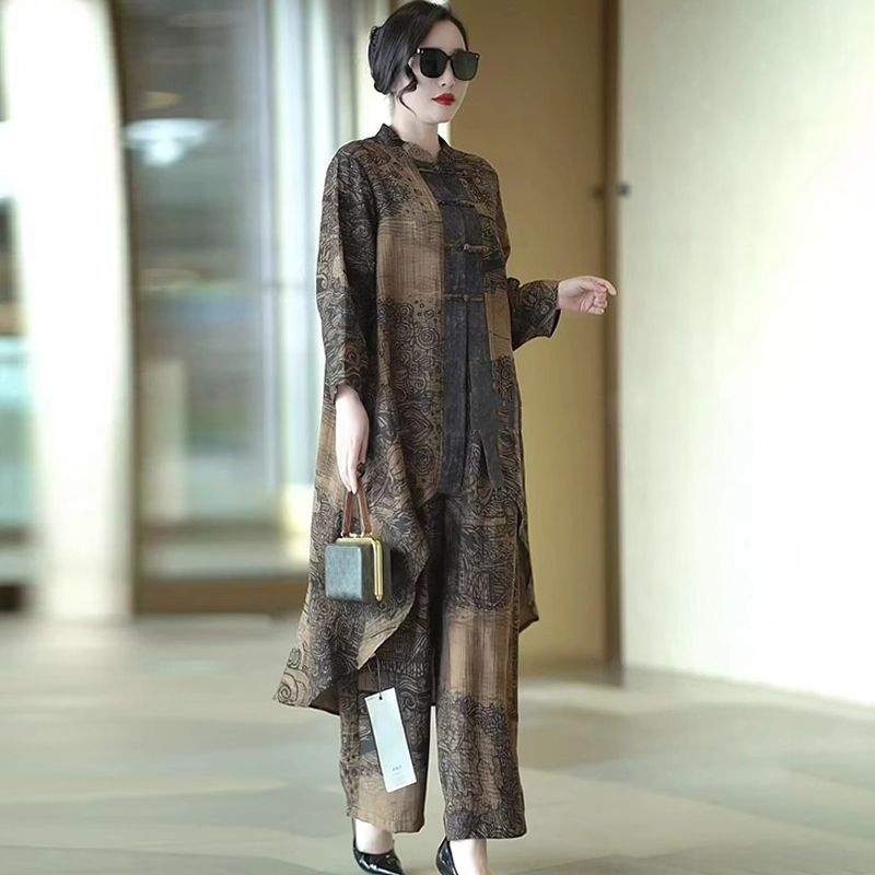 A woman models a three-piece matching set featuring a long-sleeve button-up jacket, wide-leg pants, and a matching head scarf. The set has a brown and black abstract pattern with a subtle sheen.