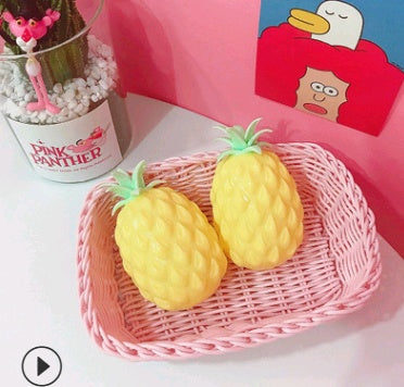 Two pineapple-shaped squishy on a pink woven tray with a colorful background