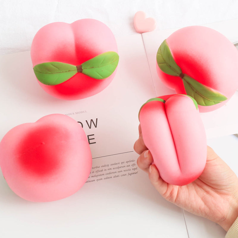 Pink peach-shaped squishies with green leaves on a white surface.