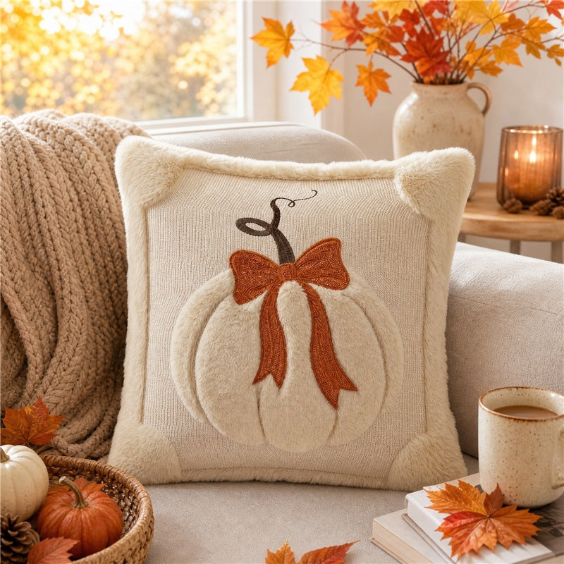 Decorative pillow with pumpkin and bow design on a couch with autumn decorations.