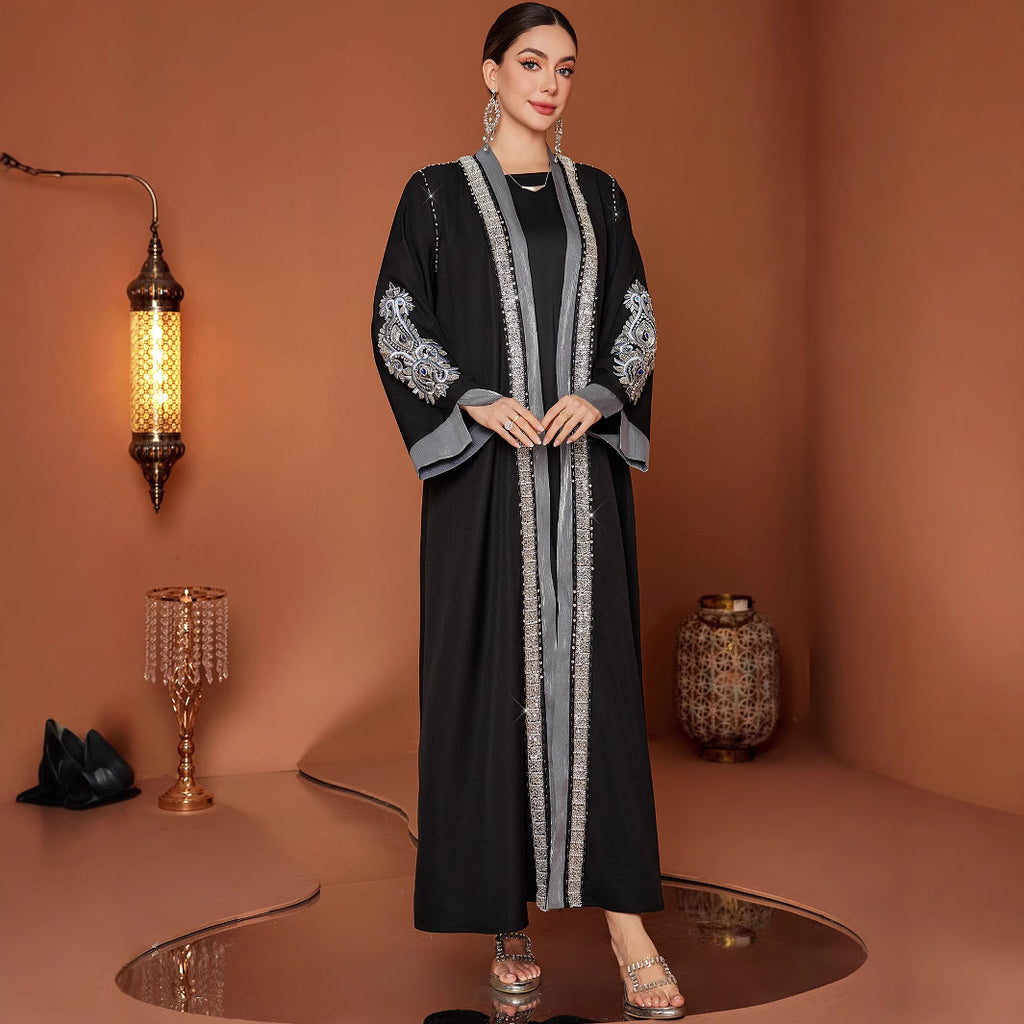 Woman wearing a black and gray abaya with intricate designs in a warm-toned room.