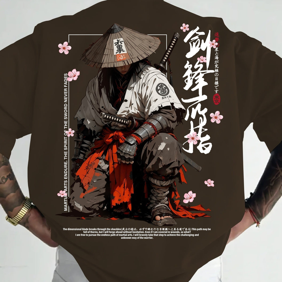A dark brown t-shirt featuring a large graphic print of a samurai in a conical hat with pink cherry blossoms and Japanese calligraphy, shown on a model's torso.