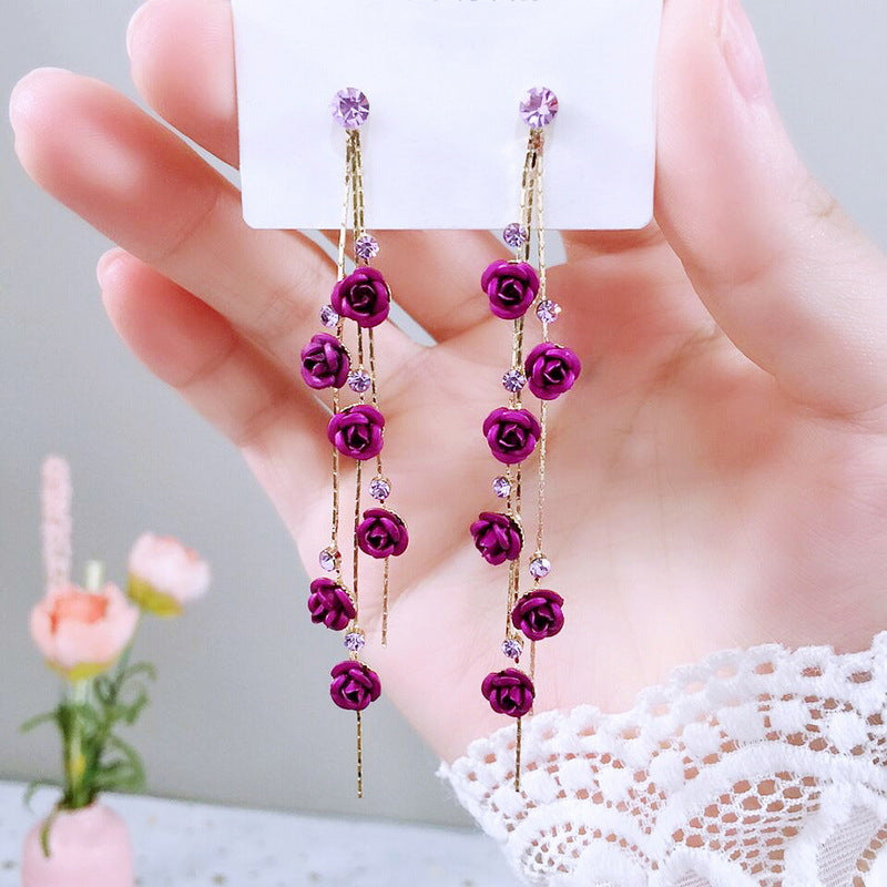 Purple rose earrings on a white card held by a hand with a blurred floral background