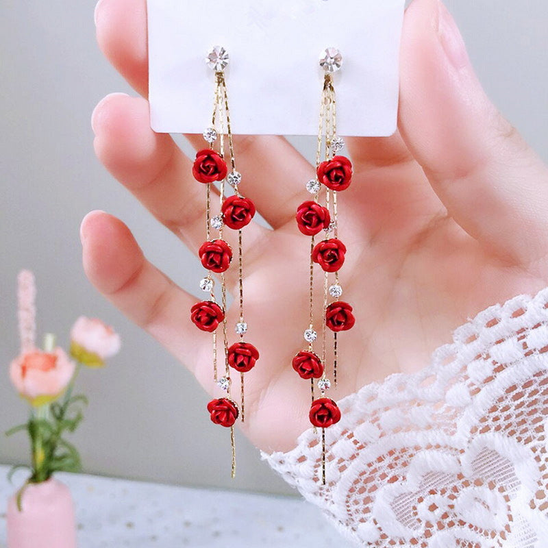 Red rose earrings held by a hand with a blurred background