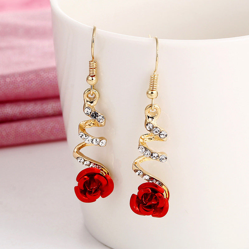 Gold earrings with red rose charms on a white background