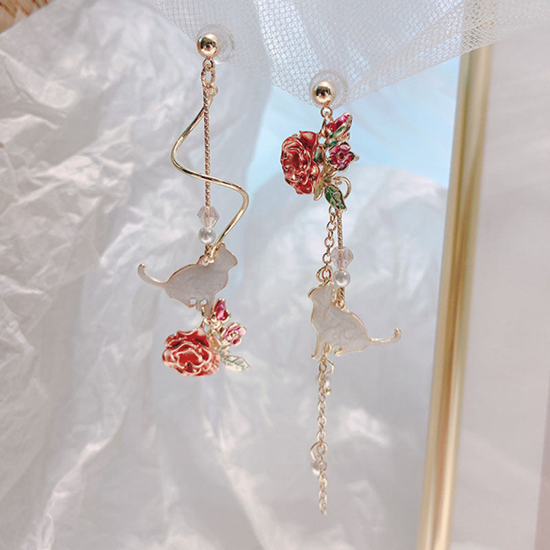 Elegant earrings with floral and cat designs on a soft fabric background