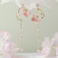 Delicate floral earrings with pink flowers and gold accents on a soft green background.