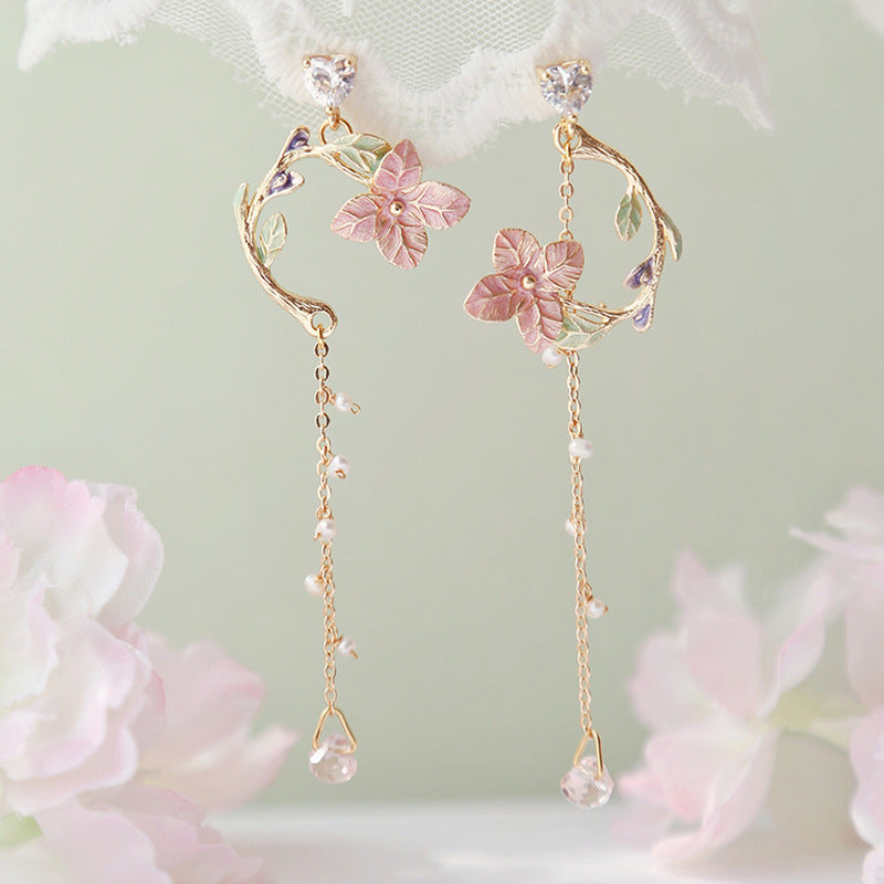 Delicate floral earrings with pink flowers and gold accents on a soft green background.