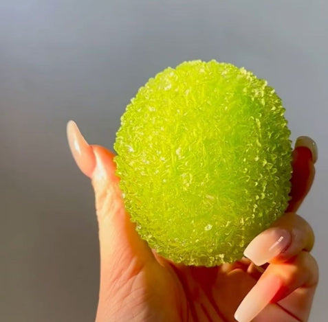 Hand holding a green textured ball Squishy against a neutral background