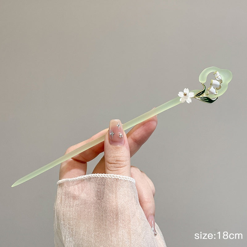 Hand holding a green jade tool with floral design against a gray background