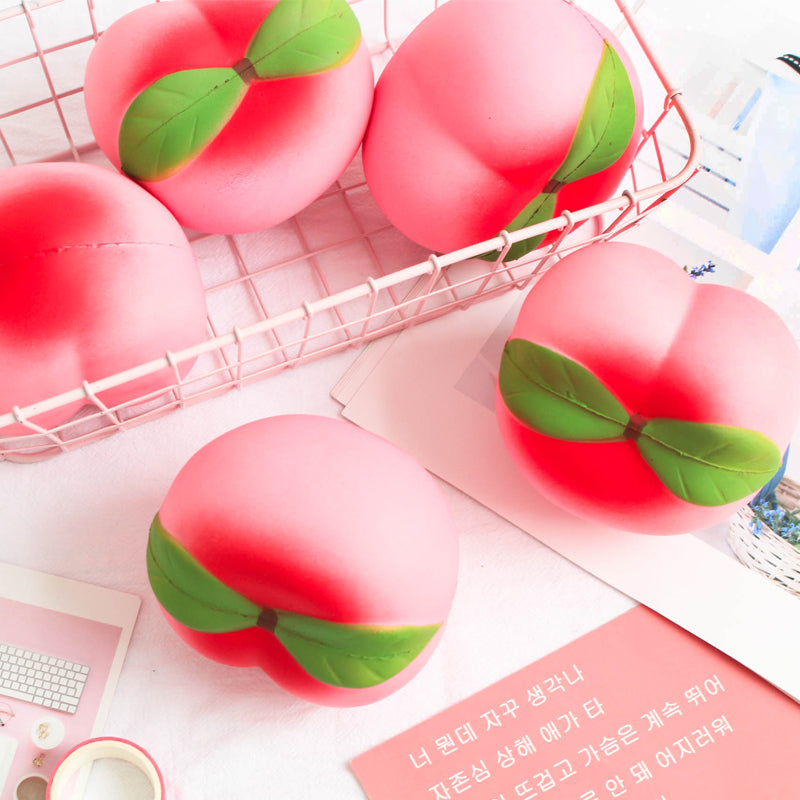 Pink peach-shaped Squishes with green leaves on a white surface.