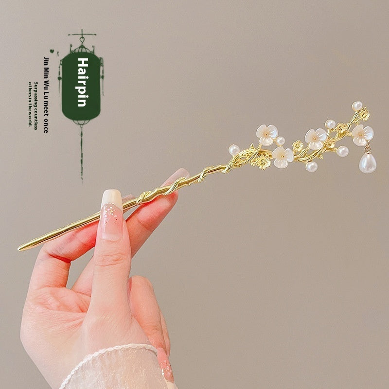 Gold hairpin with floral design held by a hand against a beige background