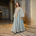 Woman in a long, elegant dress with gold accents standing in an opulent hallway.