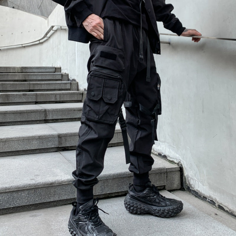 Person wearing black tactical pants and shoes standing on a staircase.