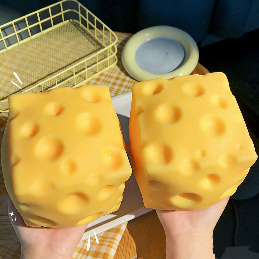 Two large yellow cheese cubes squishy held by hands with a checkered tablecloth and basket in the background.