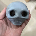 Small skull squishy fidget toy stress relief held in a hand against a neutral background