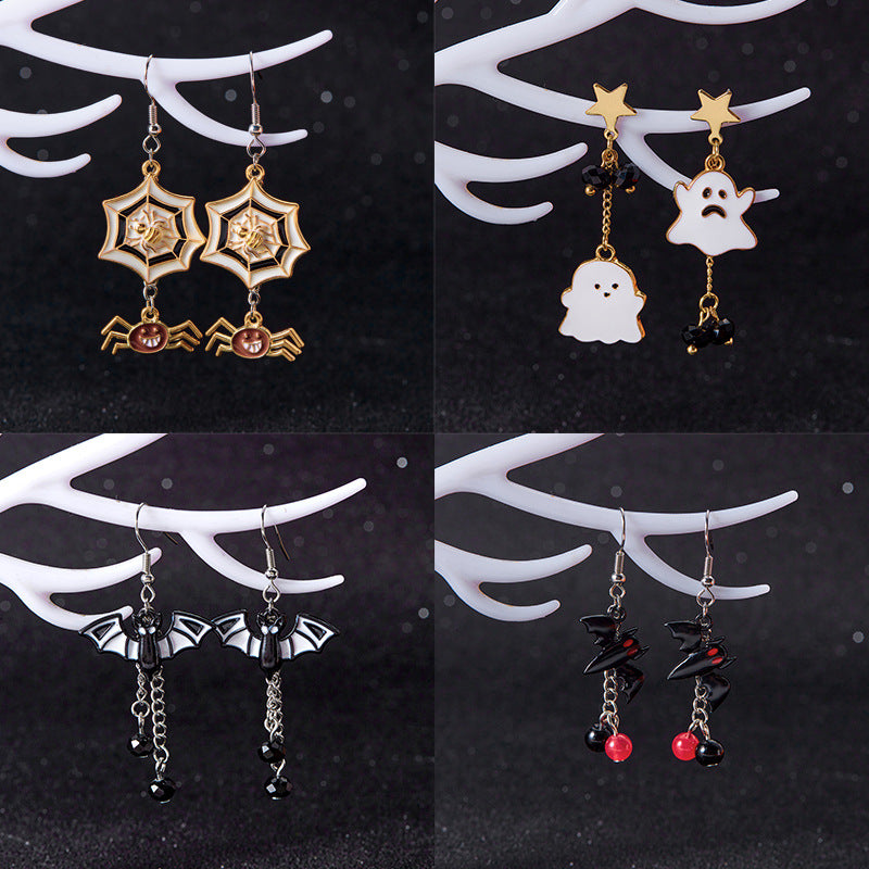 Four pairs of Halloween-themed dangling earrings displayed on white branch-shaped stands against a dark background. The designs include gold spiderwebs with black spiders, white ghosts with black details, black bats with silver chains, and black lightning bolts with red beads.