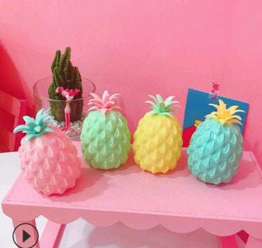 Colorful pineapple-shaped squishy toys on a pink table against a pink wall.