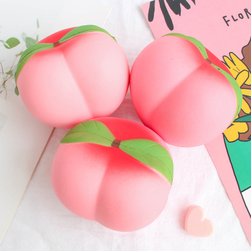 Three peach-shaped Squishy on a white background with a colorful book partially visible.