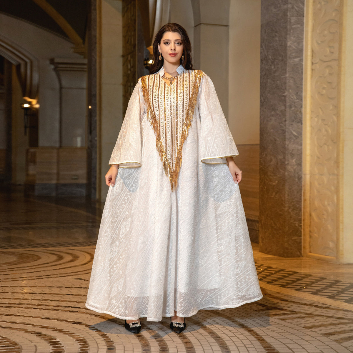 Woman in a long, elegant white dress with gold accents standing in an ornate hallway.