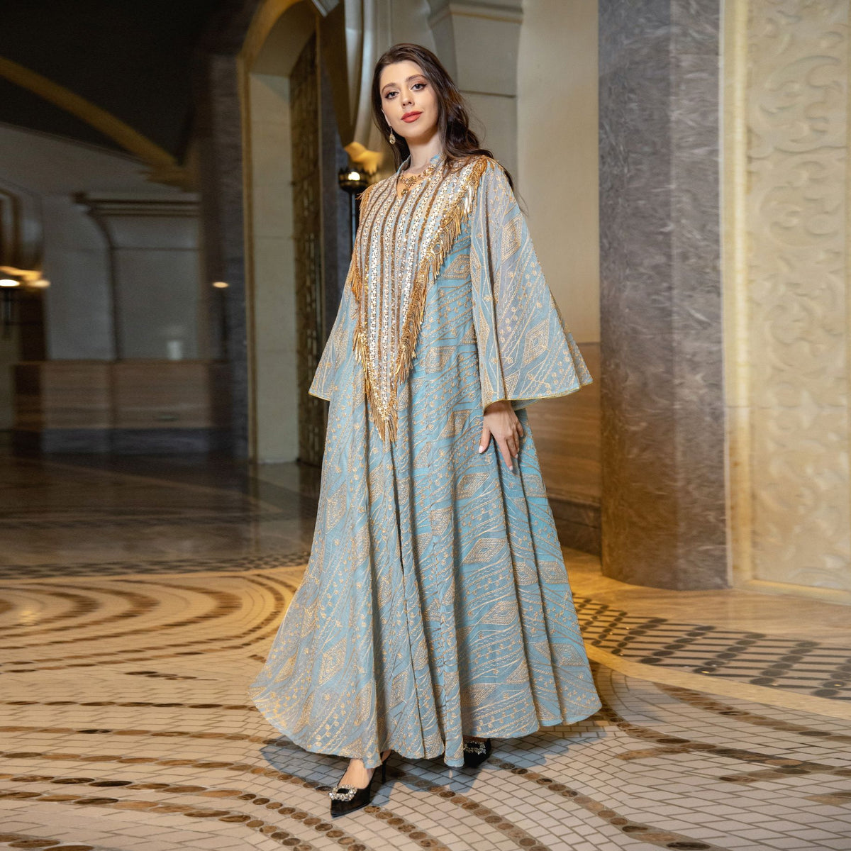 Woman in a long, elegant dress with gold accents standing in an opulent hallway.