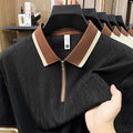 Black sweater with brown and beige collar held by a hand, with a blurred indoor background.