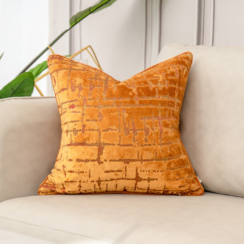 Orange textured pillow on a beige sofa with a plant in the background