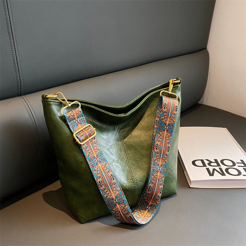 Green handbag with a patterned strap on a gray surface
