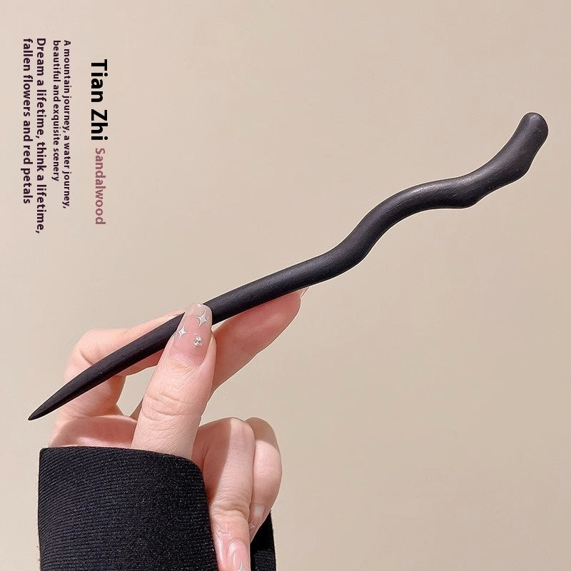 Hand holding a sandalwood hairpin against a beige background