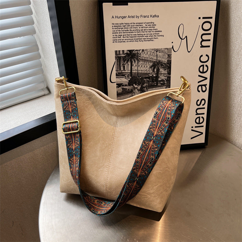Beige handbag with patterned strap on a surface next to a book titled 'Viens avec moi'.