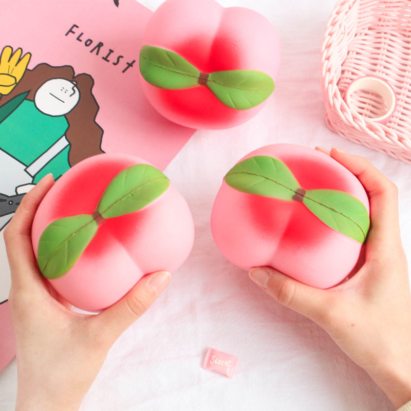 Two pink peach-shaped squishes held by hands with a cartoon character and basket in the background.