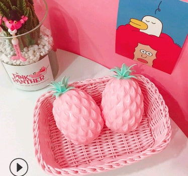 Pink Pineapple squishy toys with green tops in a wicker basket on a pink background.
