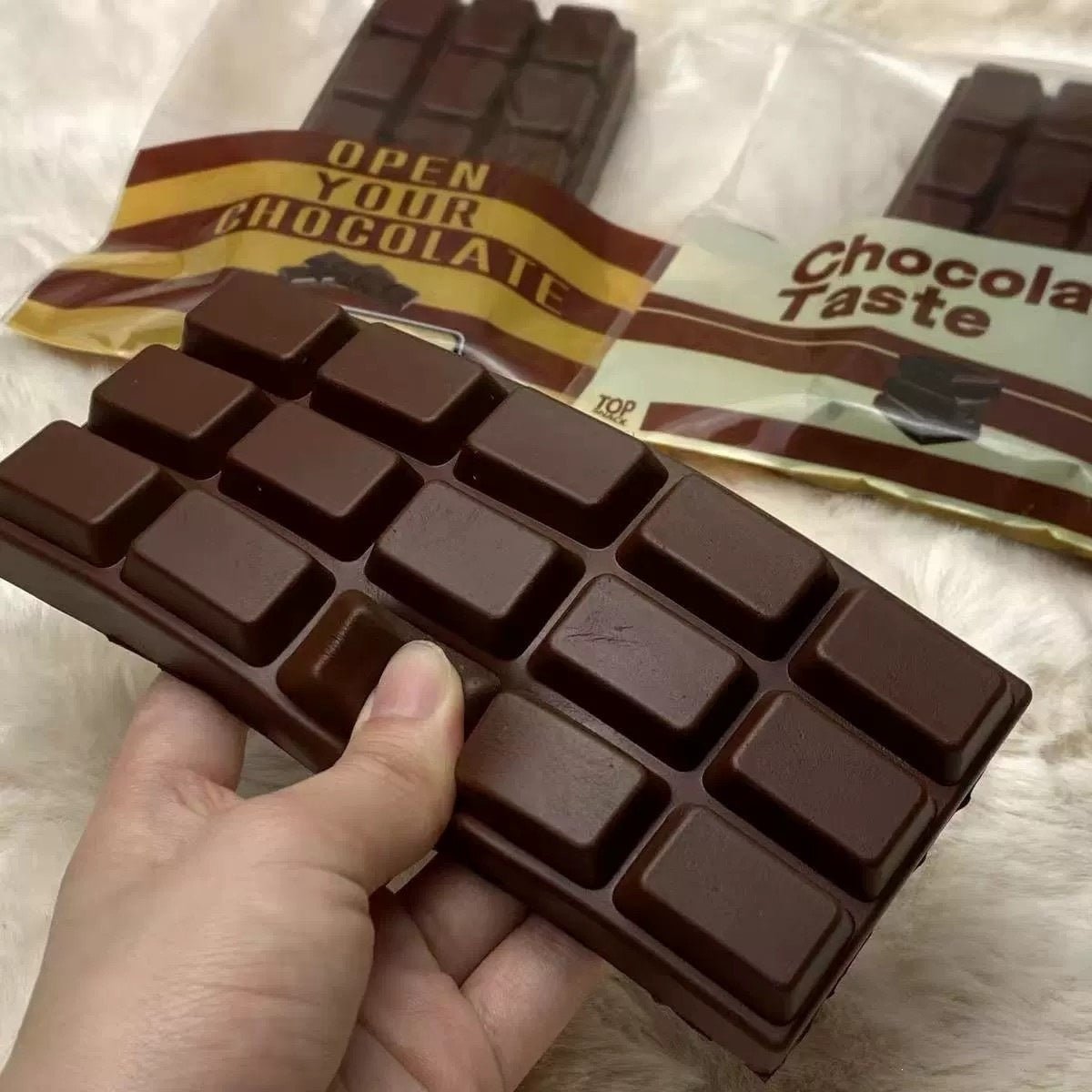 Chocolate bar squishy with packaging labeled 'Open Your Chocolate' and 'Chocola Taste' on a textured surface.