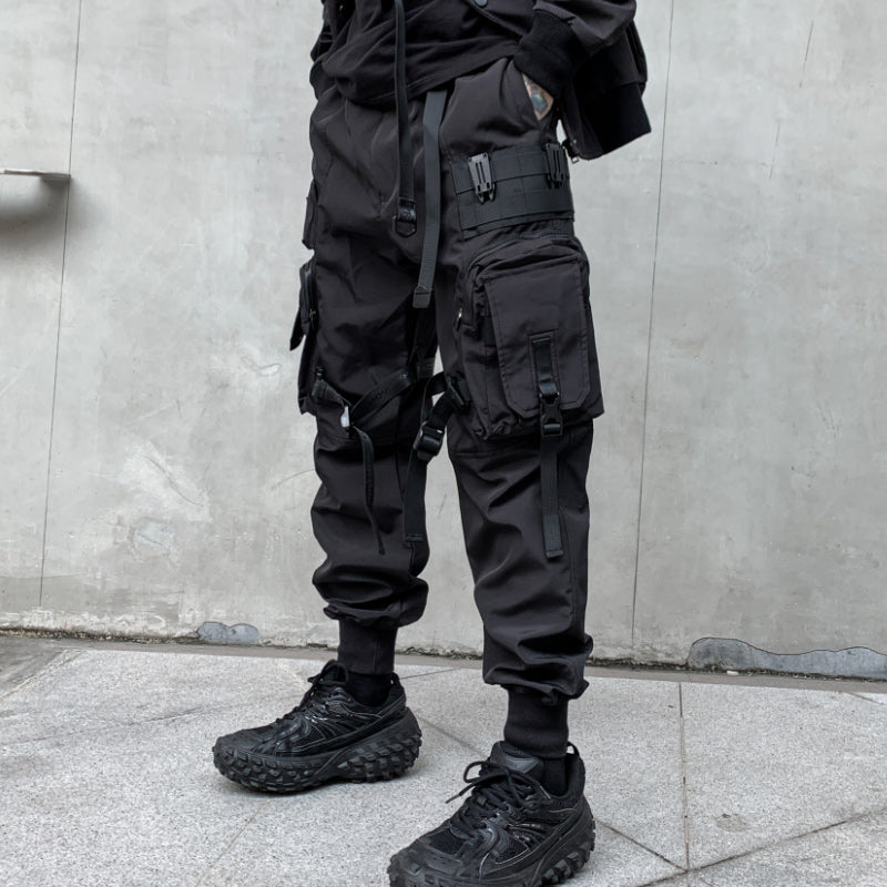 Person wearing black tactical pants and boots against a gray wall.