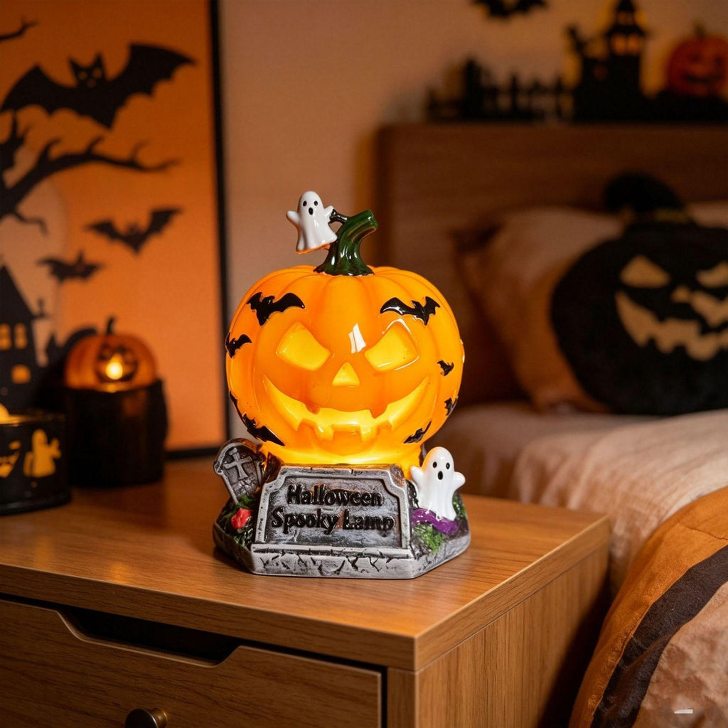 A Halloween-themed jack-o'-lantern night light with a glowing orange pumpkin face, small white ghosts, and a tombstone base reading 'Halloween Spooky Camp,' placed on a wooden bedside table in a bedroom setting.