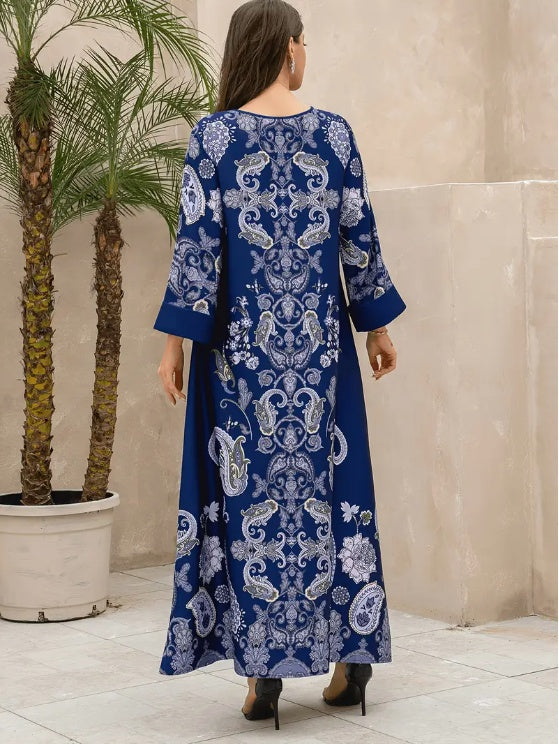 Woman wearing a blue and white patterned dress standing in a room with a plant and tiled floor.