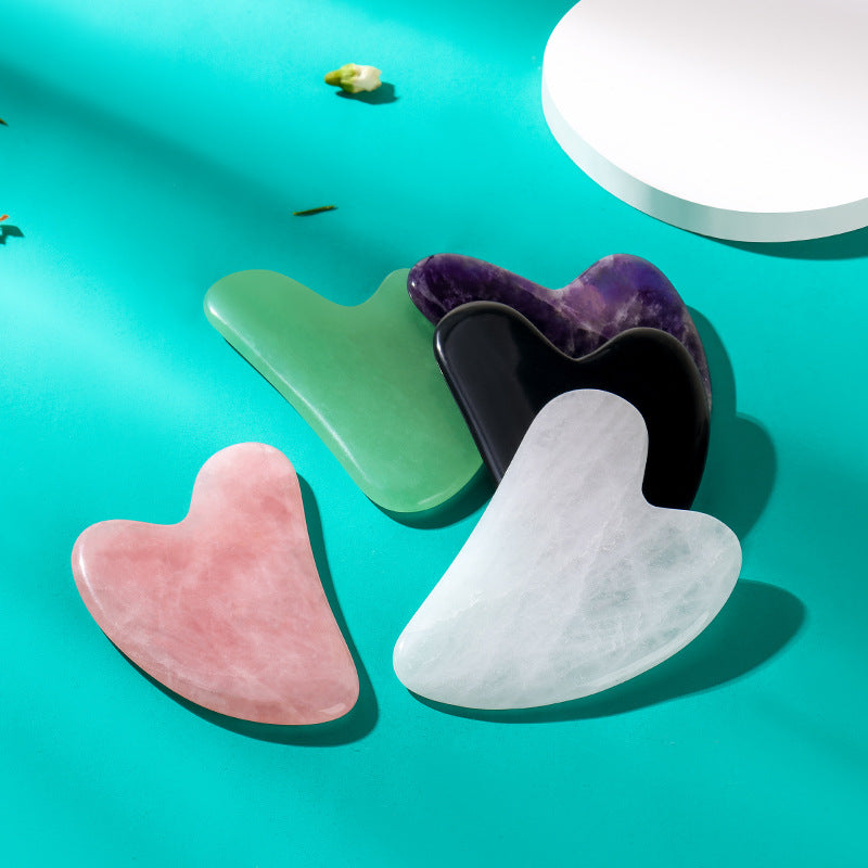 Four gua sha tools in different colors on a teal background
