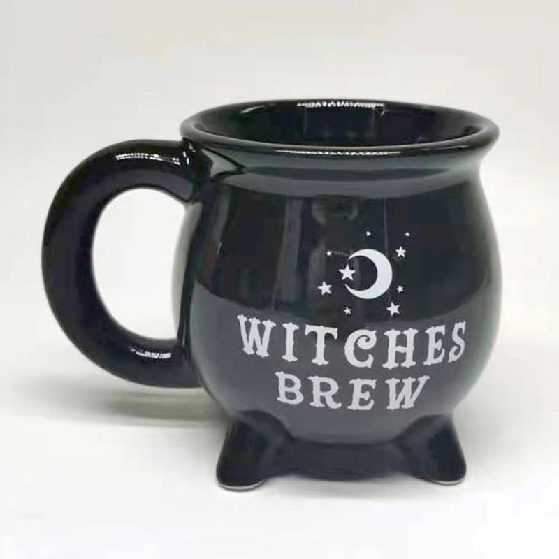 A glossy black cauldron-shaped mug with a white crescent moon and stars graphic and the words 'WITCHES BREW' printed on the front, set against a plain light background.