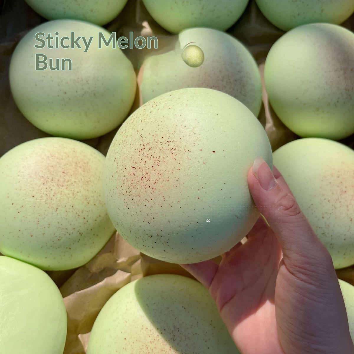 Hand holding a green sticky melon bun with more buns in the background.