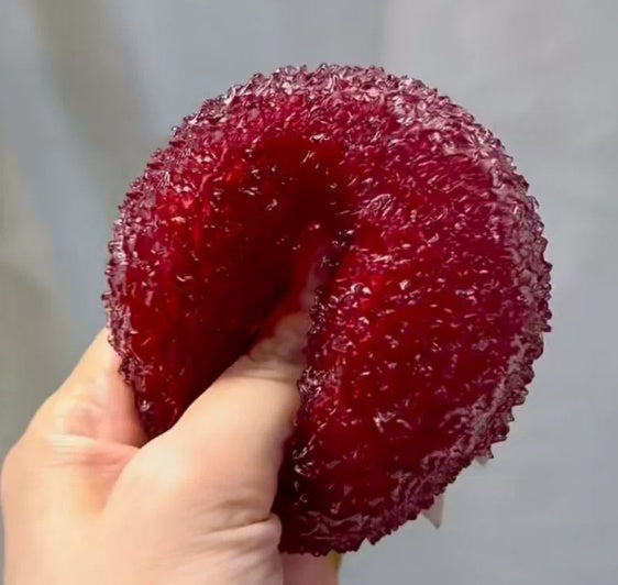 Hand holding a red, textured ball Squishy against a neutral background