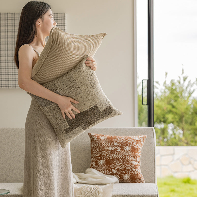 Woman holding a textured pillow in a living room with another pillow on a sofa.