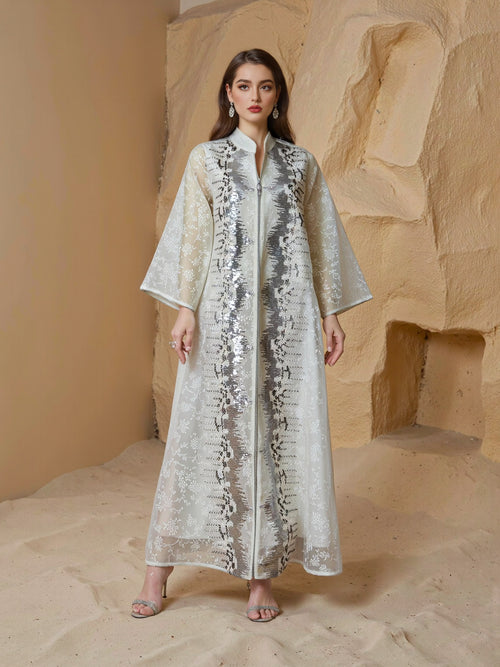 Woman wearing a long, light-colored dress with sequin detailing against a stone wall.