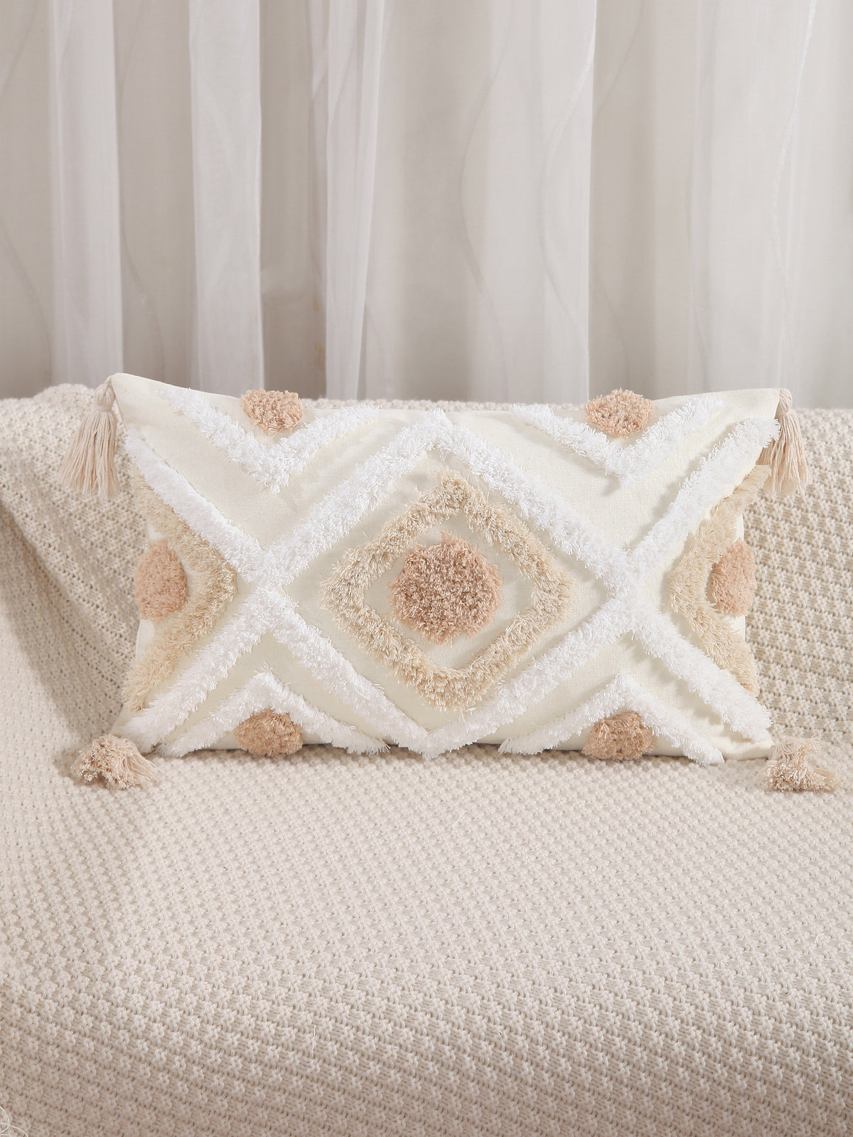 Decorative pillow with geometric pattern and pom-poms on a beige couch.