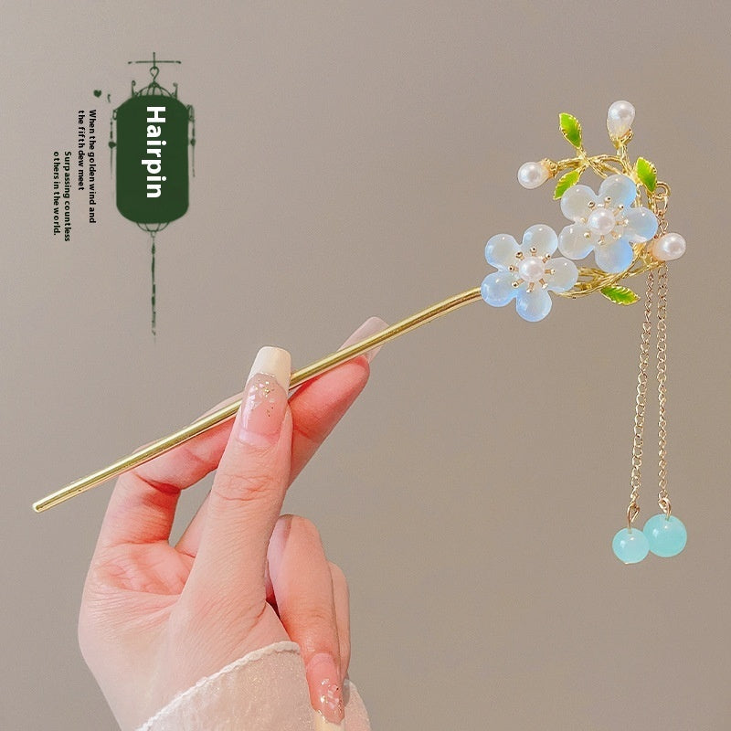 Decorative hairpin with floral design held by a hand against a neutral background