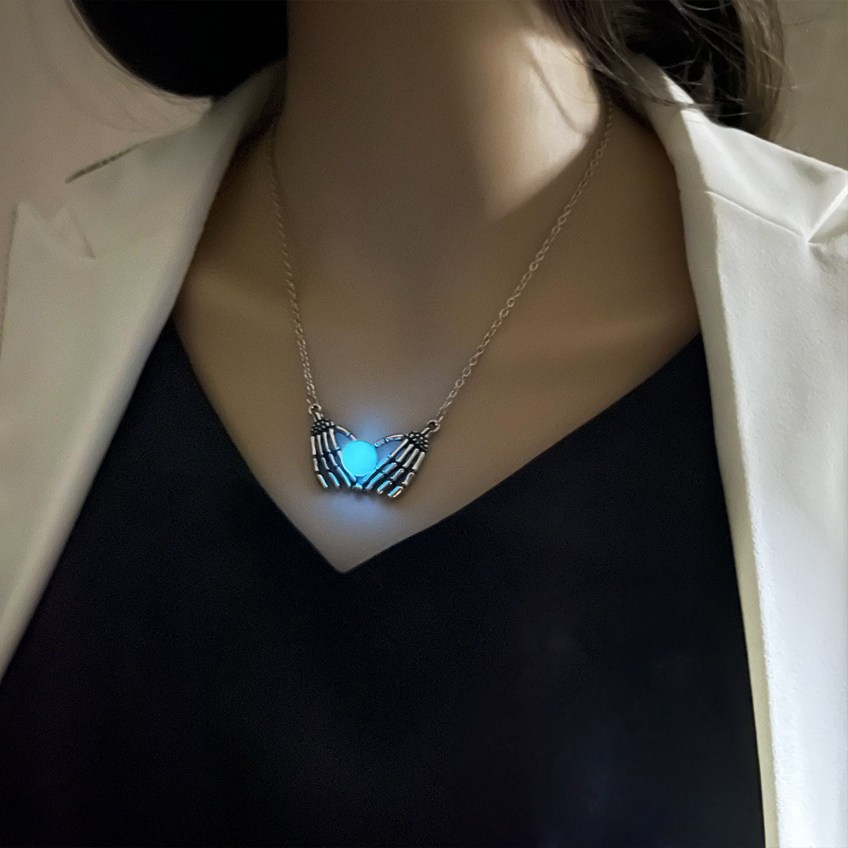 Necklace with a glowing blue pendant worn by a person in a white jacket.