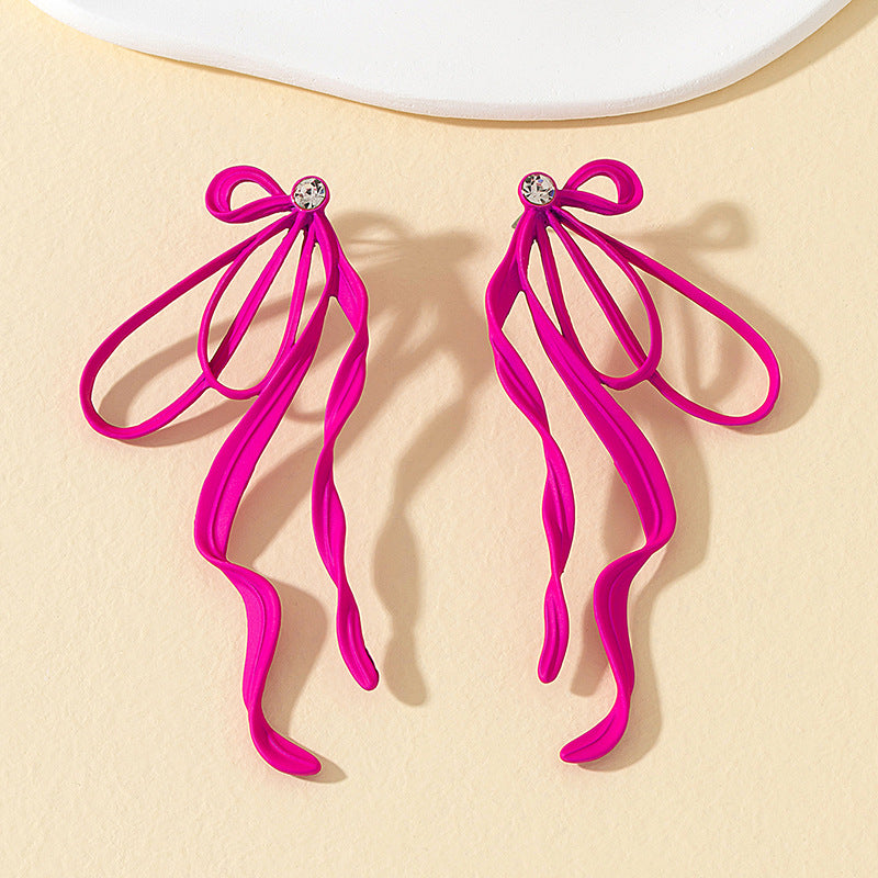 Pair of pink bow-shaped earrings on a beige background