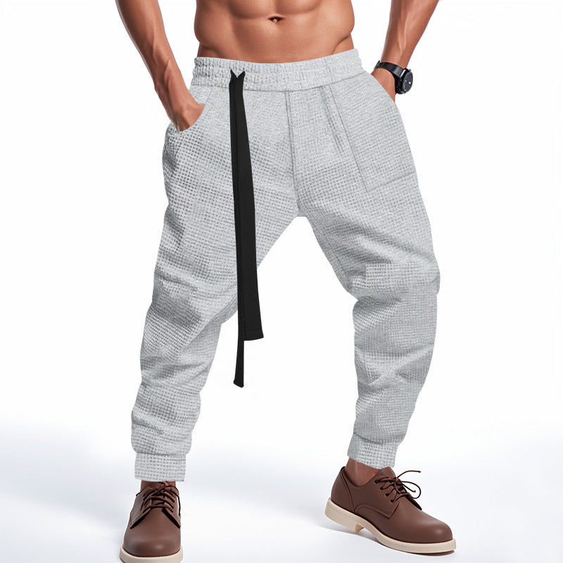 Person wearing gray checkered pants with a black strap on a white background