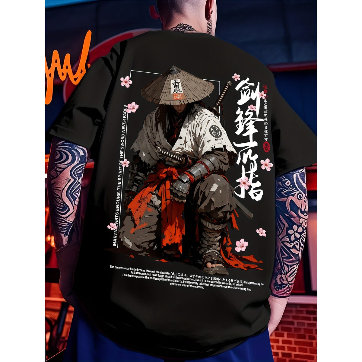 A person shown from behind wearing a black graphic T-shirt with a large samurai illustration on the back, featuring white Japanese characters, pink cherry blossoms, and red/orange accents. The background is a dimly lit, moody urban setting.